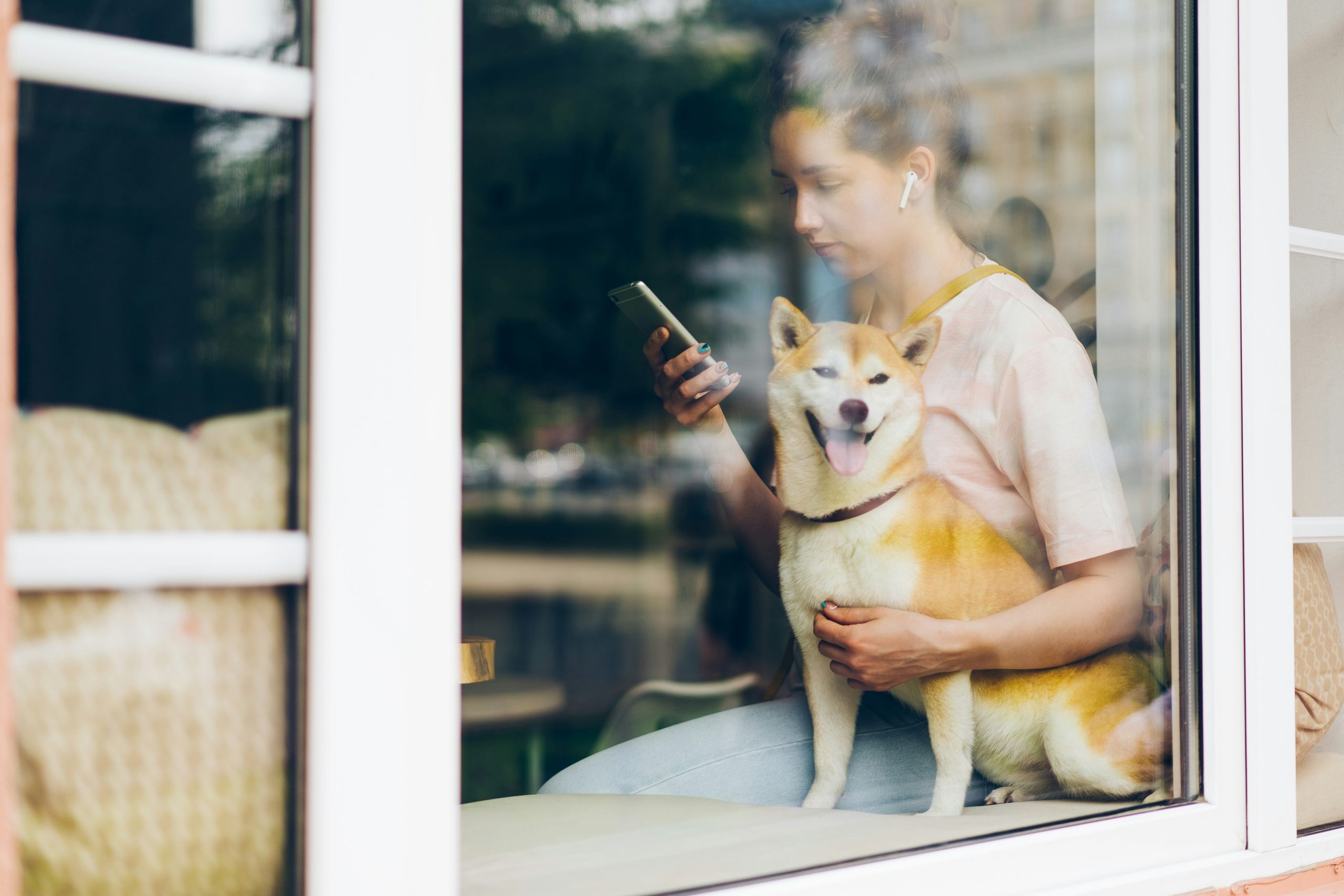 Pet owner smiling while holding her dog and using a smartphone app.